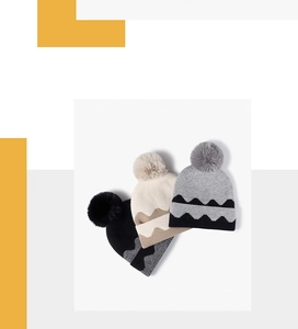 Close-up of three knitted beanies with pom-poms in black, beige, and grey colors