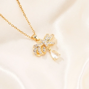 Elegant gold bow necklace with sparkling zircon and pear-shaped pendant on silk backdrop