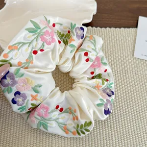 Detail of embroidered flowers on satin scrunchie with soft pastel colors and textures
