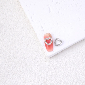 Detailed close-up of hollow silver heart nail charms with rhinestones on a pink base