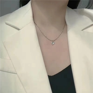 Detail of a minimalist heart pendant necklace on a model wearing an elegant office blazer