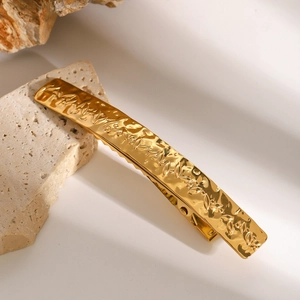 Golden stainless steel hair clip with leaf engraving on a beige travertine stone