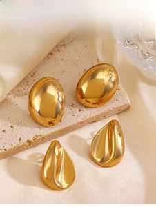 Macro detail of polished gold drop earrings and oval studs on stone and silk background