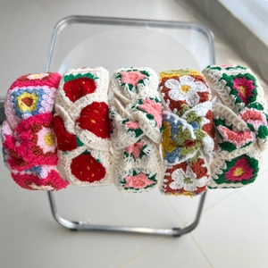 Close-up of five handmade knitted headbands featuring floral and strawberry embroidery patterns