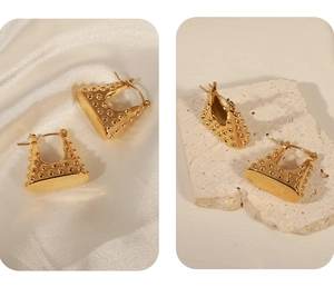 Close-up of golden geometric hollow handbag earrings with textured bead surface finish