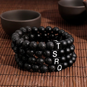 Macro view of four-piece black volcanic rock and matte bead bracelets with letter charms