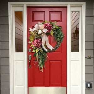 Detail of a floral wreath with pink hydrangeas and a beige burlap bow on a red door