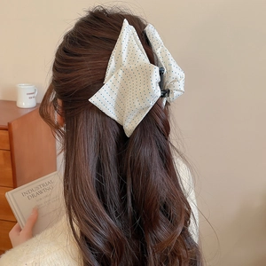 Close-up of a large white fabric bow hair claw clip with blue polka dots on long hair