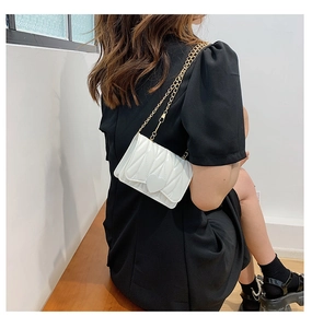 Detail of white quilted crossbody bag with heart motif and gold chain on model