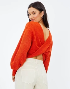 Dettaglio del maglione in maglia arancione senza schienale con un elegante design incrociato