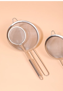 Overhead view of two stainless steel mesh strainers on a peach-colored background