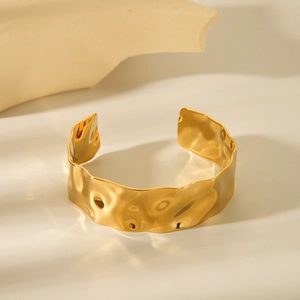 Dettaglio del bracciale rigido dorato largo con texture martellata e ondulata unica