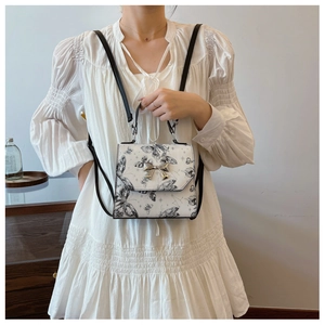 Detail of white leather backpack with black butterfly print and silver bow clasp