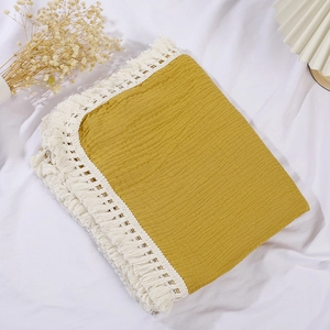 Ginger yellow cotton gauze baby blanket with white tassels on a cozy white background