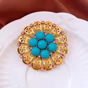 Vintage gold floral brooch with turquoise beads and pink rhinestones on a white plate