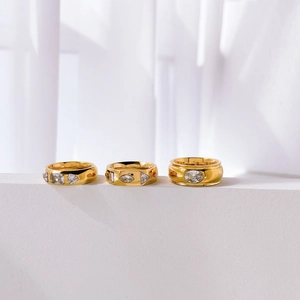 Polished gold-plated wide band rings with inlaid zircons on a white marble stand