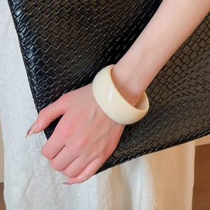 Detail of a minimalist cream resin acrylic wide bangle worn on a female wrist