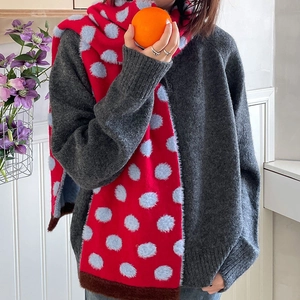 Detail of red knitted scarf with blue fluffy polka dots worn by a model in soft lighting
