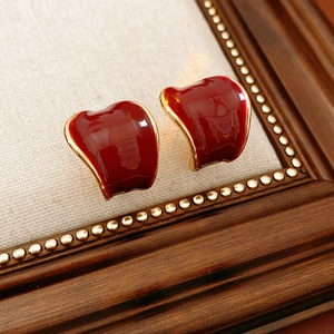 Dettaglio degli orecchini a C in smalto rosso placcati oro su tessuto beige testurizzato