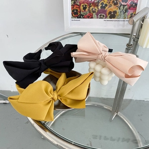 Detailed view of large fabric bow headbands in black, pink, and yellow on a glass table