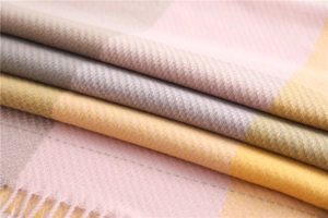 Detailed close-up of soft pink and grey plaid scarf fabric with tassel fringe