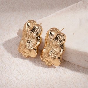 Detailed macro shot of golden lava-textured irregular geometric metal stud earrings