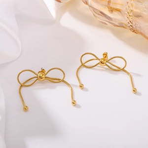 Gold bow earrings with woven texture on white fabric and glass bottle background