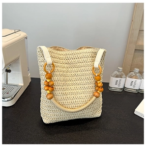 Detail of beige straw bucket bag with decorative wooden beads and woven rope handle