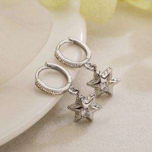 Boucles d'oreilles créoles étoiles en argent avec zircons sur un plateau en céramique