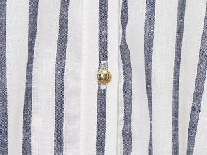Dettaglio macro della camicia in lino a righe blu e bianche con bottone dorato