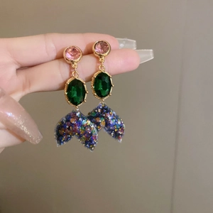 Close-up of mermaid tail earrings with pink and green gems and sparkling colorful sequins