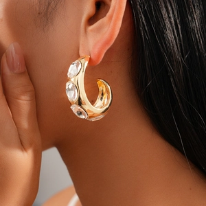 Close-up of gold C-shaped earring with three clear rhinestones on model's ear