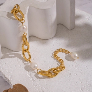 Bracciale a catena dorata con perle barocche bianche su una superficie in pietra ruvida