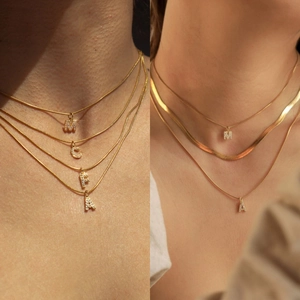 Detail of layered gold-tone chains featuring zircon-encrusted M, C, F, and A pendants
