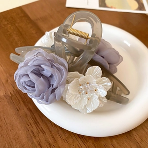 Detail of elegant translucent grey hair claw with cloth roses and white floral accents