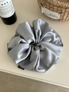 Detail of silver blue oversized satin scrunchie with fashion label on white table