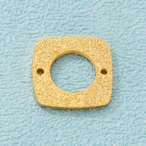 Macro detail of gold frosted geometric pendant with central hole on textured background