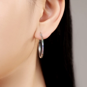 Gros plan d'une boucle d'oreille en argent avec zircons arc-en-ciel portée par un modèle