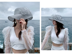 Detail of grey sun hat with decorative mesh flowers shown on a seaside beach background
