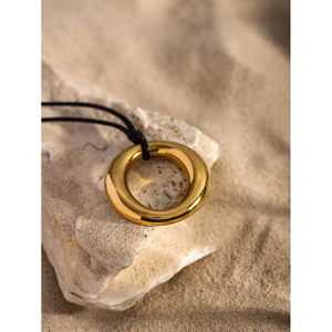 Close-up of a chunky gold 18k plated circular pendant on a black cord over natural stone