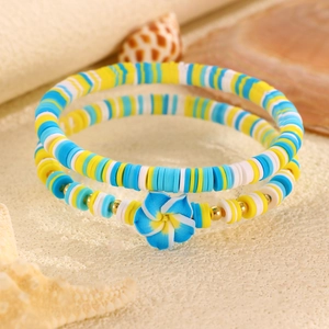 Vista macro di perle di plumeria blu e braccialetti in argilla a tema oceano sulla spiaggia