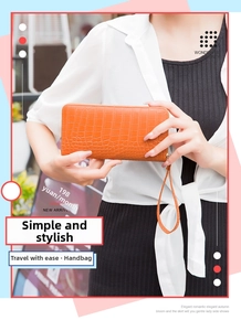Detail of orange crocodile pattern long wallet featuring a gold zipper and wrist strap
