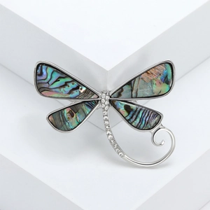 Silver dragonfly brooch with colorful abalone shell and rhinestones on white pedestal