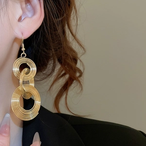 Detailed close-up of model wearing gold triple spiral ring drop earrings with hook