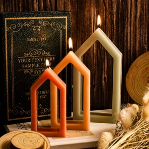 Three hollow house-shaped decorative candles in various sizes on a rustic wooden desk