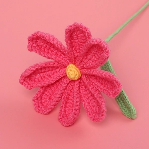 Close-up of pink crochet cosmos flower with yellow core and green leaves on pink backdrop