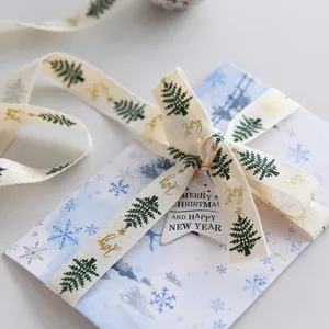 Christmas cotton ribbon with green trees and gold Joy print tied to a snowflake card