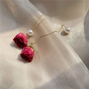 Macro detail of red rose bud earrings with white pearls and delicate gold chains