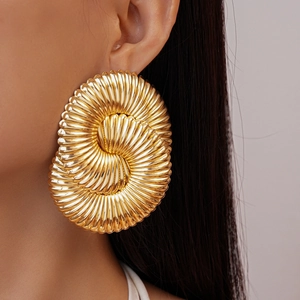 Détail d'une boucle d'oreille spirale dorée imposante portée sur l'oreille d'un modèle