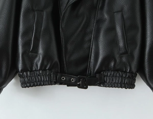 Detail der schwarzen Lederjacke mit Metallschnallengürtel und elastischem Saum am Bund